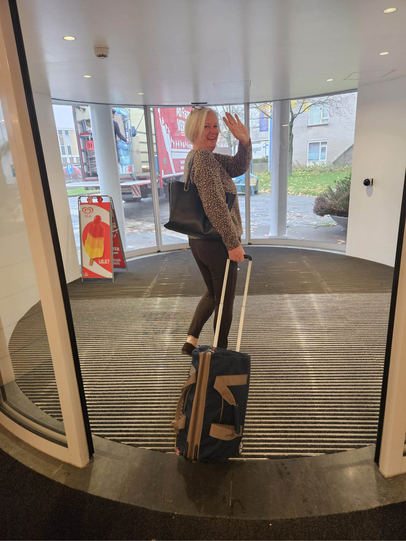 A woman is standing in a hallway with a suitcase, smiling and waving. AI generated content