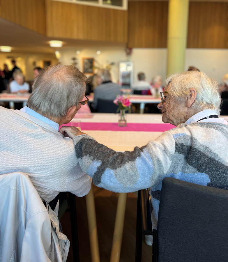 Two elderly people are sitting at a table, one of them is wearing glasses. AI generated content