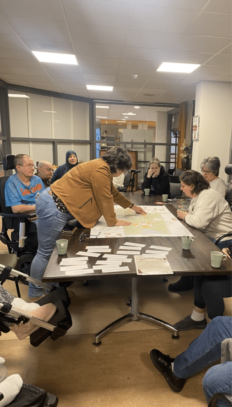 A group of people are gathered around a table with a map on it. They are sitting on chairs and engaging in conversation. There are several cups on the table, and a potted plant is visible in the background. AI generated content