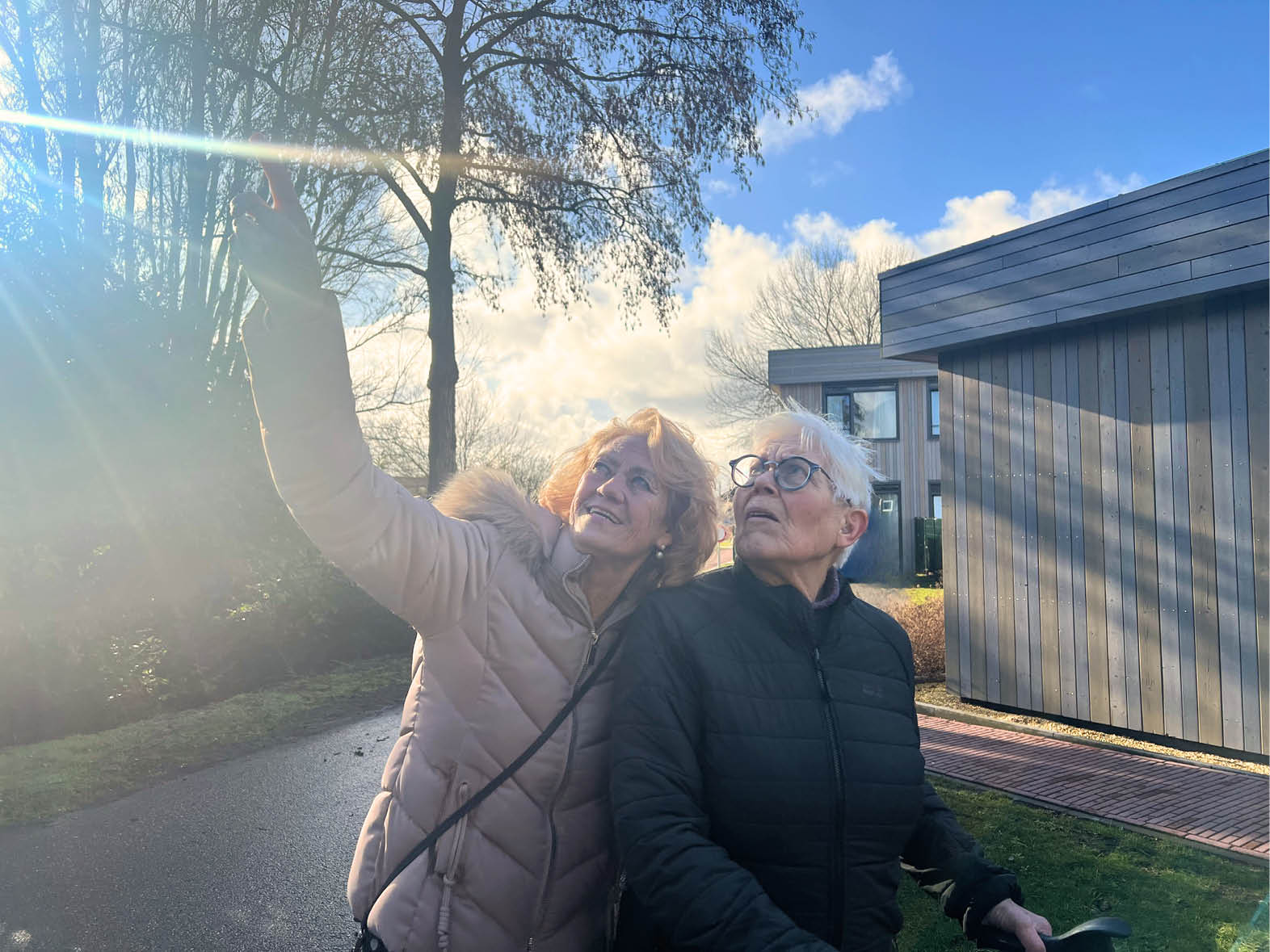 Two women are standing outside, one of them is holding a cell phone up to the sky. AI generated content