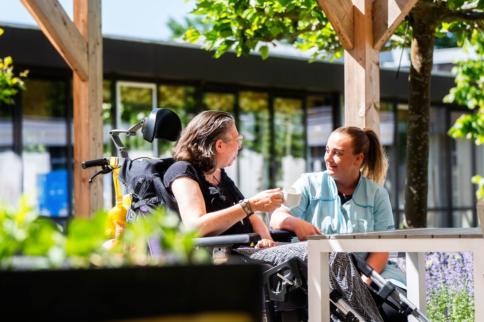 Two women are sitting at a table, one of them in a wheelchair. They are drinking coffee from cups. AI generated content