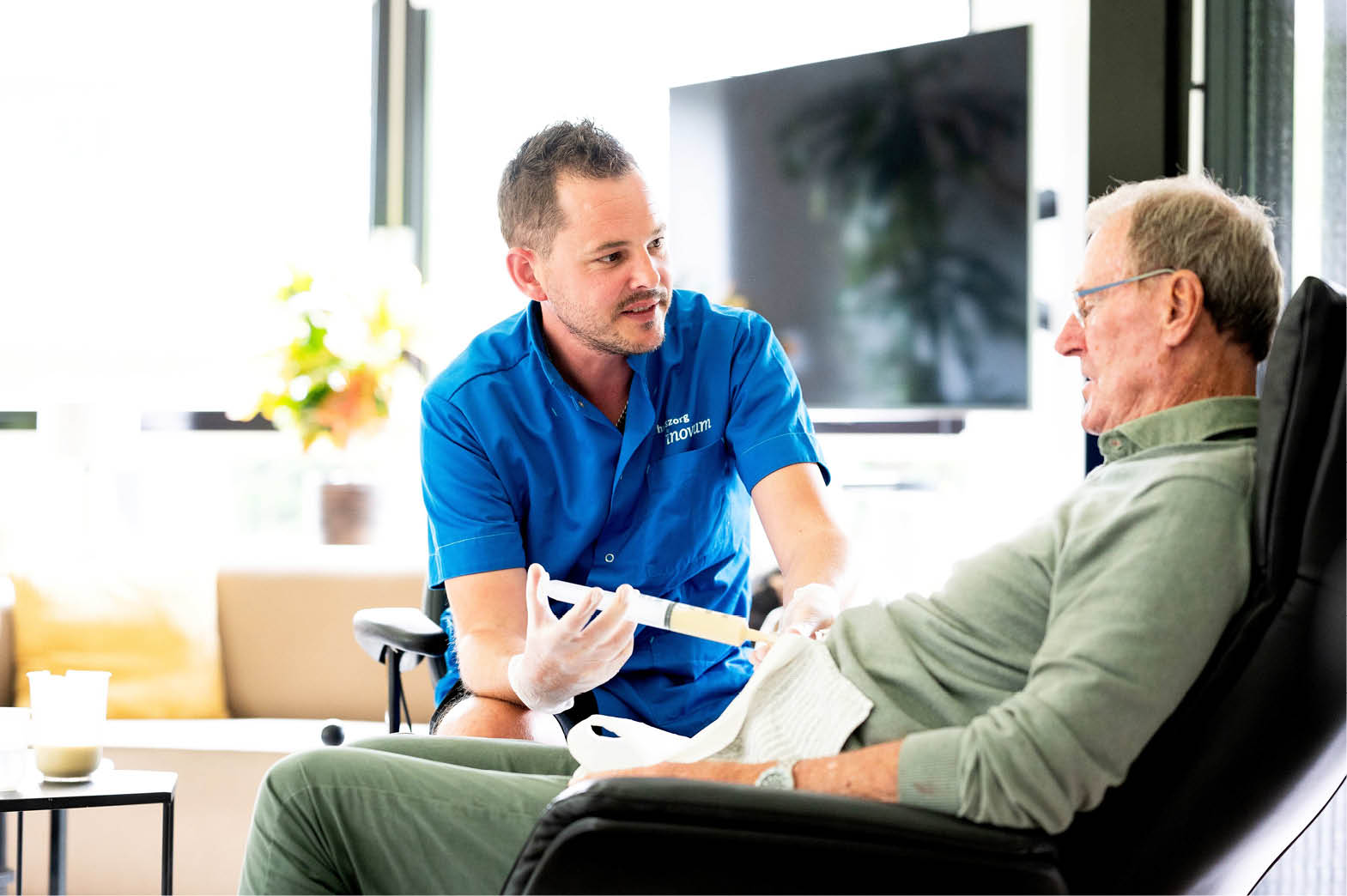 A man is sitting in a chair while a nurse or doctor attends to him. The man is wearing glasses. AI generated content